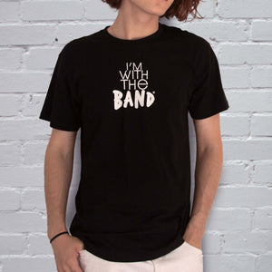 I'm With The Band® logo T-shirt with white print on black T being worn by a cool young man standing against a white painted brick wall