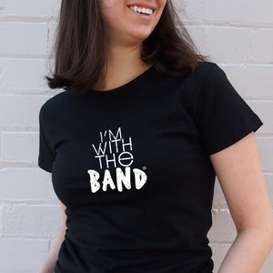 I'm With The Band® white logo print on black close-fit women's T-shirt very close up view on smiling young woman standing in front of a painted brick wall