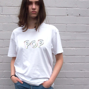 I'm With The Band® Bubble Pop T-shirt with iridescent white print on white T being worn by a cool young woman standing against a white painted brick wall