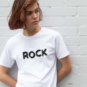 I'm With The Band® Bubble Rock T-shirt with bubble slick black print on white T being worn by a cool young man standing against a white painted brick wall