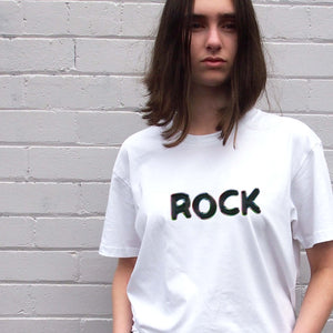 I'm With The Band® Bubble Rock T-shirt with bubble slick black print on white T being worn by a cool young woman standing against a white painted brick wall