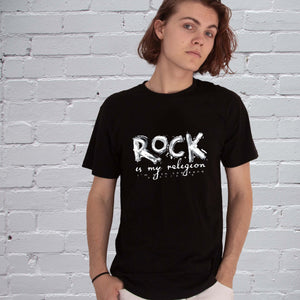 Rock Is My Religion T-shirt by I'm With The Band® with original hand-painted white graphic print on black T being worn by a cool young man standing against a white painted brick wall