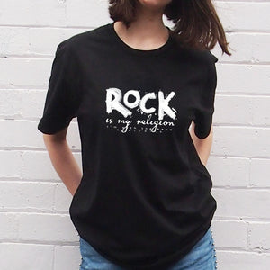 Rock Is My Religion T-shirt byI'm With The Band® with original hand-painted white graphic print on black T being worn by a young woman standing against a white painted brick wall