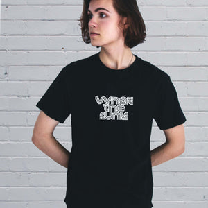 I'm With The Band® What The Funk T-shirt with white print on black T  on a cool young man standing against a painted brick wall