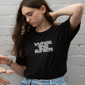 I'm With The Band® What The Funk T-shirt with white print on black T  on a cool young woman standing in front of a painted brick wall